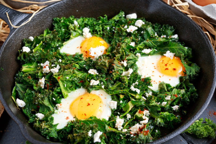 Homemade Green Kale with eggs, feta cheese, herbs in iron pan. healthy rustic breakfast