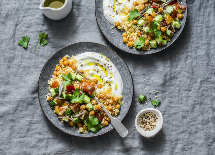 Spiced chickpeas and couscous with shepherd's salad and greek yogurt on a grey background, top view. Healthy vegetarian food