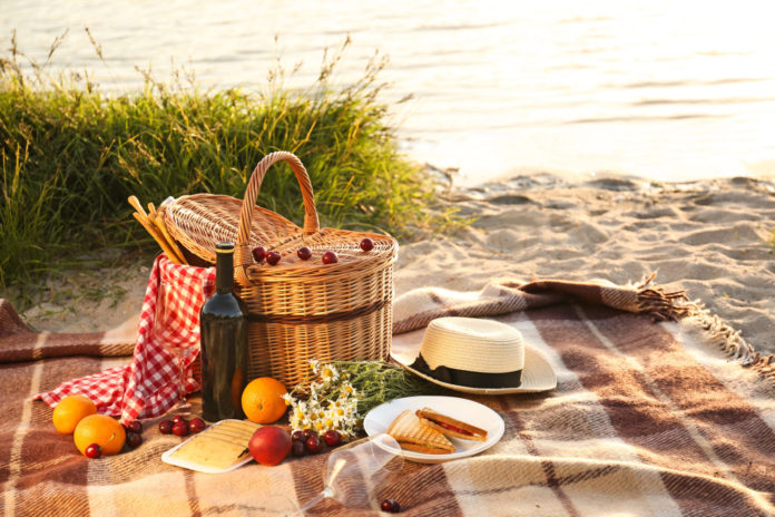 Wicker basket with tasty food and drink for romantic picnic near