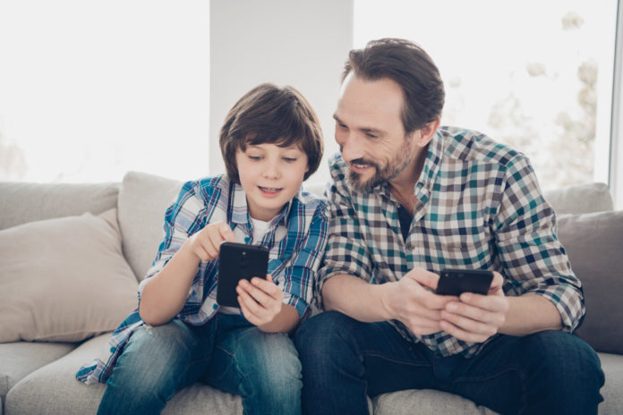 Younger generation and digital devices gadgets concept. Photo of smart clever understands how to use modern technology shows screen of his telephone to daddy sitting on comfort divan