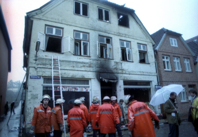 A group of fire fighters stand in front of the burnt out house in the...