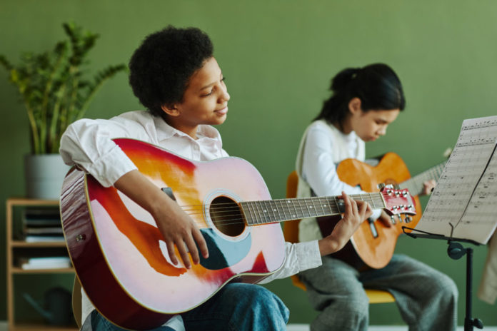 Schoolgirl with acoustic guitar looking at paper with notes on music stand