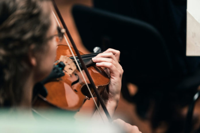 A musician playing the violin in a string section of a classical