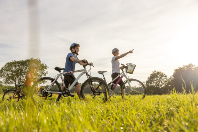 Mother points at something with her finger while she and her children pushing the bike on a country lane