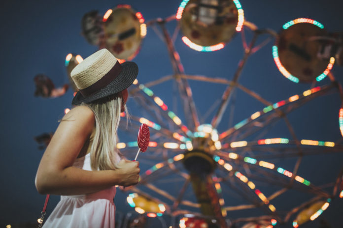 Lovely young woman holding a lollipop while looking at a Ferris wheel