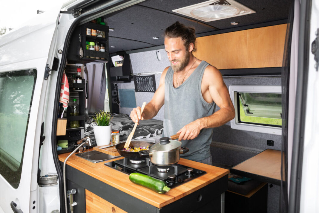 Ein Mann steht in seinem Camper und kocht sein Essen